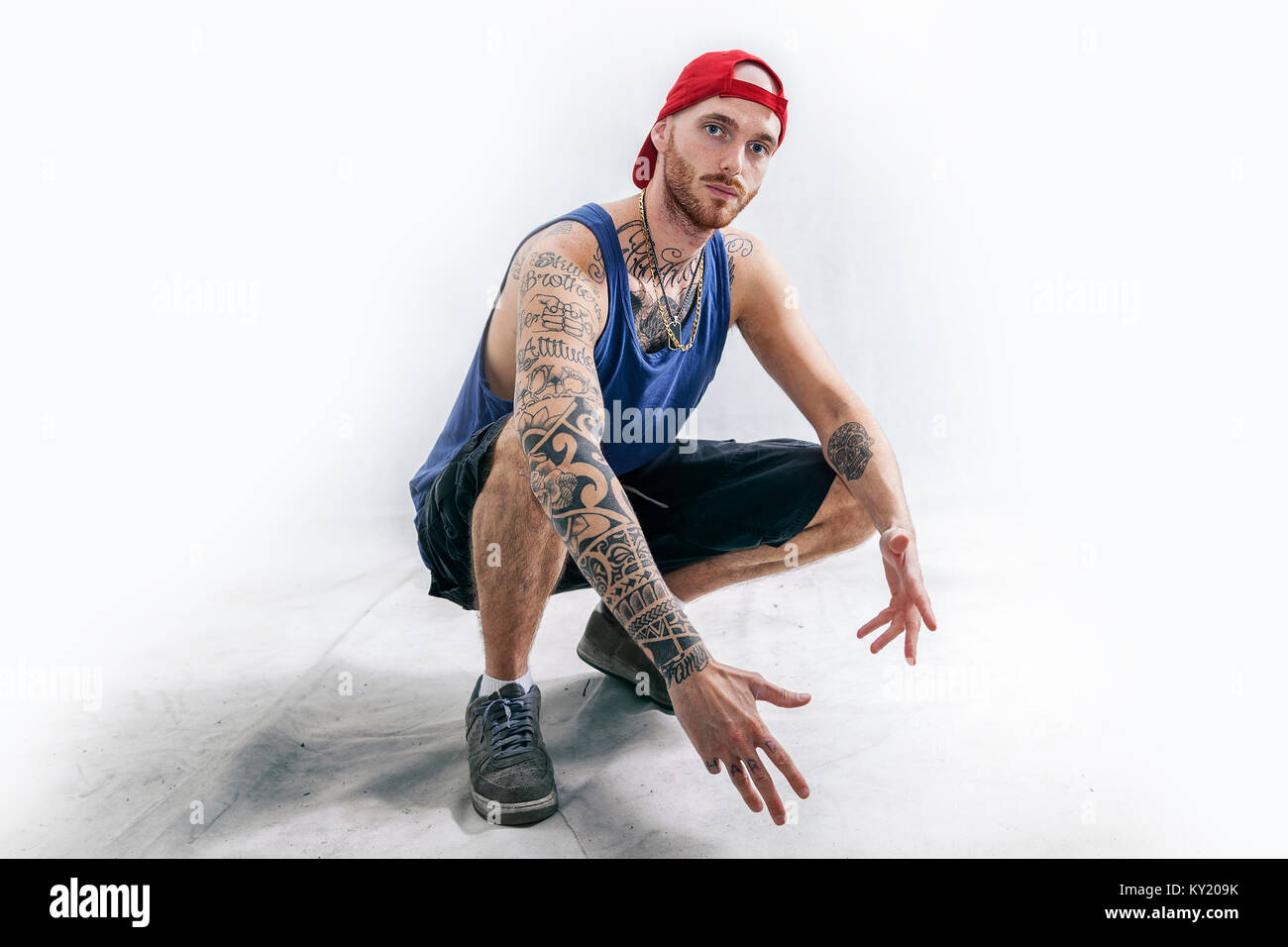sitting tattooed rap singer posing in studio with expressive position on a white background Stock Photo