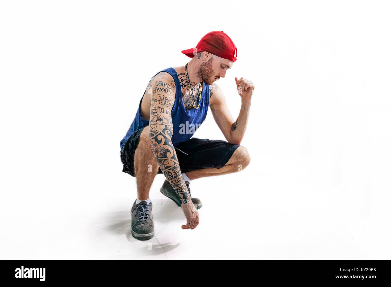 sitting tattooed rap singer posing in studio with expressive position on a white background Stock Photo