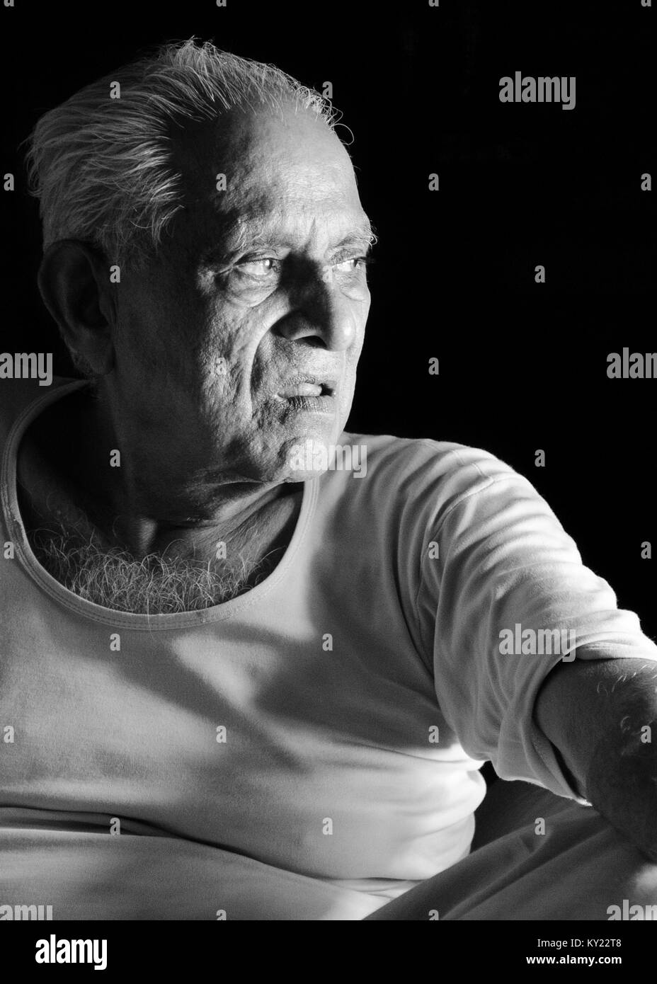 Black and white portrait of an elderly Indian man looking away, lost in thought, over black background. Stock Photo