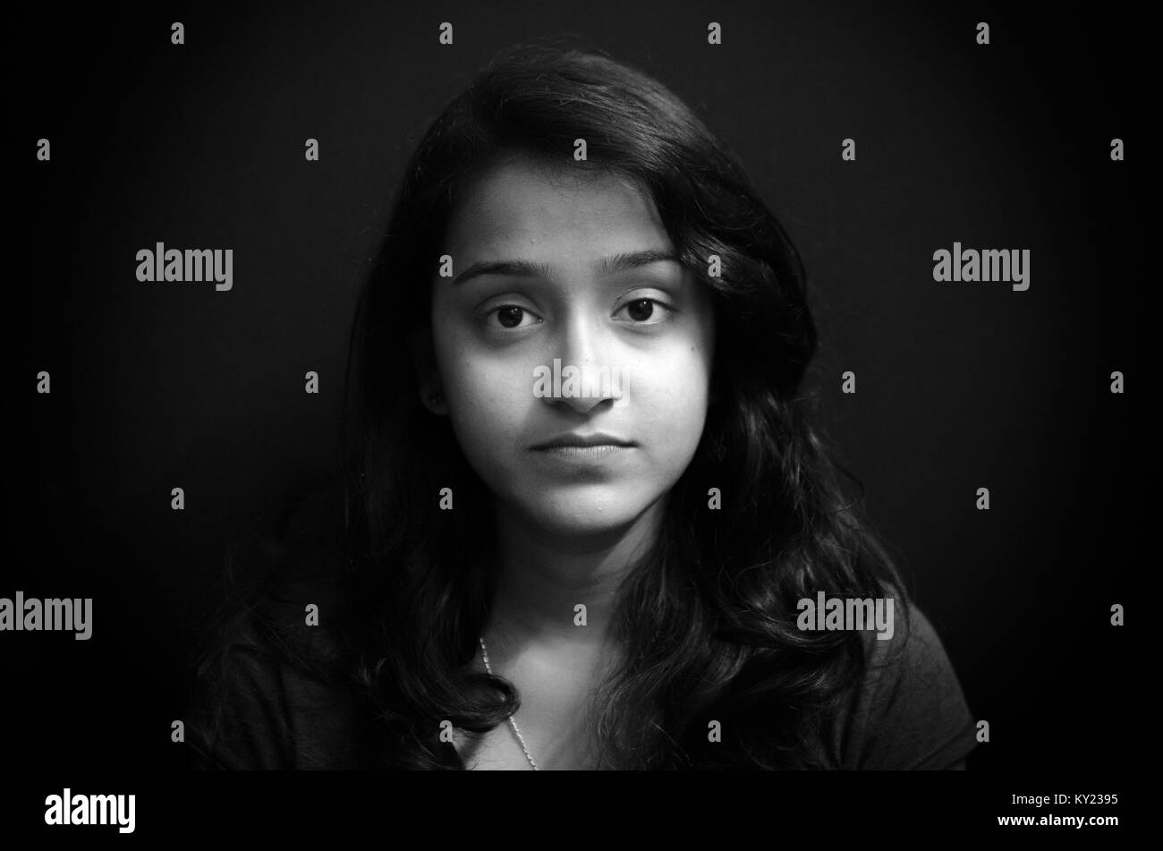 Black and white portrait of a cute, chubby Indian girl giving a blank stare over black background. Stock Photo