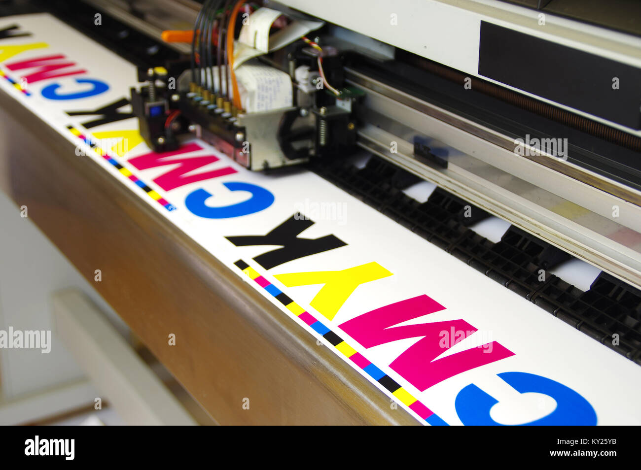 Plotter head printing CMYK test on white paper. Digital large inkjet machine working. Stock Photo
