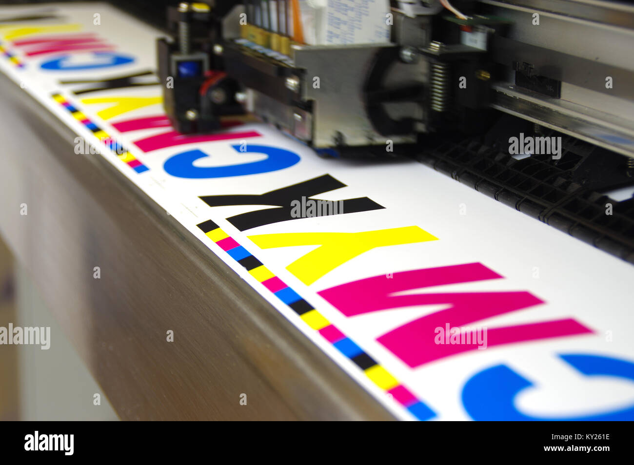 Plotter head printing CMYK test on white paper. Large digital inkjet machine work. Stock Photo