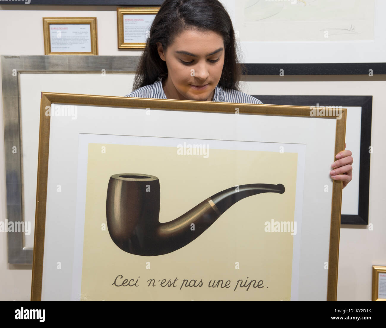 ExCel, London, UK. 12 January 2018. Behind the scenes, setting up the 3 day London Art, Antiques & Interiors Fair which brings together 60 specialist dealers showcasing over 30,000 unusual and desirable items from classic to contemporary. Member of exhibition staff examines a framed Rene Magritte lithograph. Credit: Malcolm Park/Alamy Live News. Stock Photo