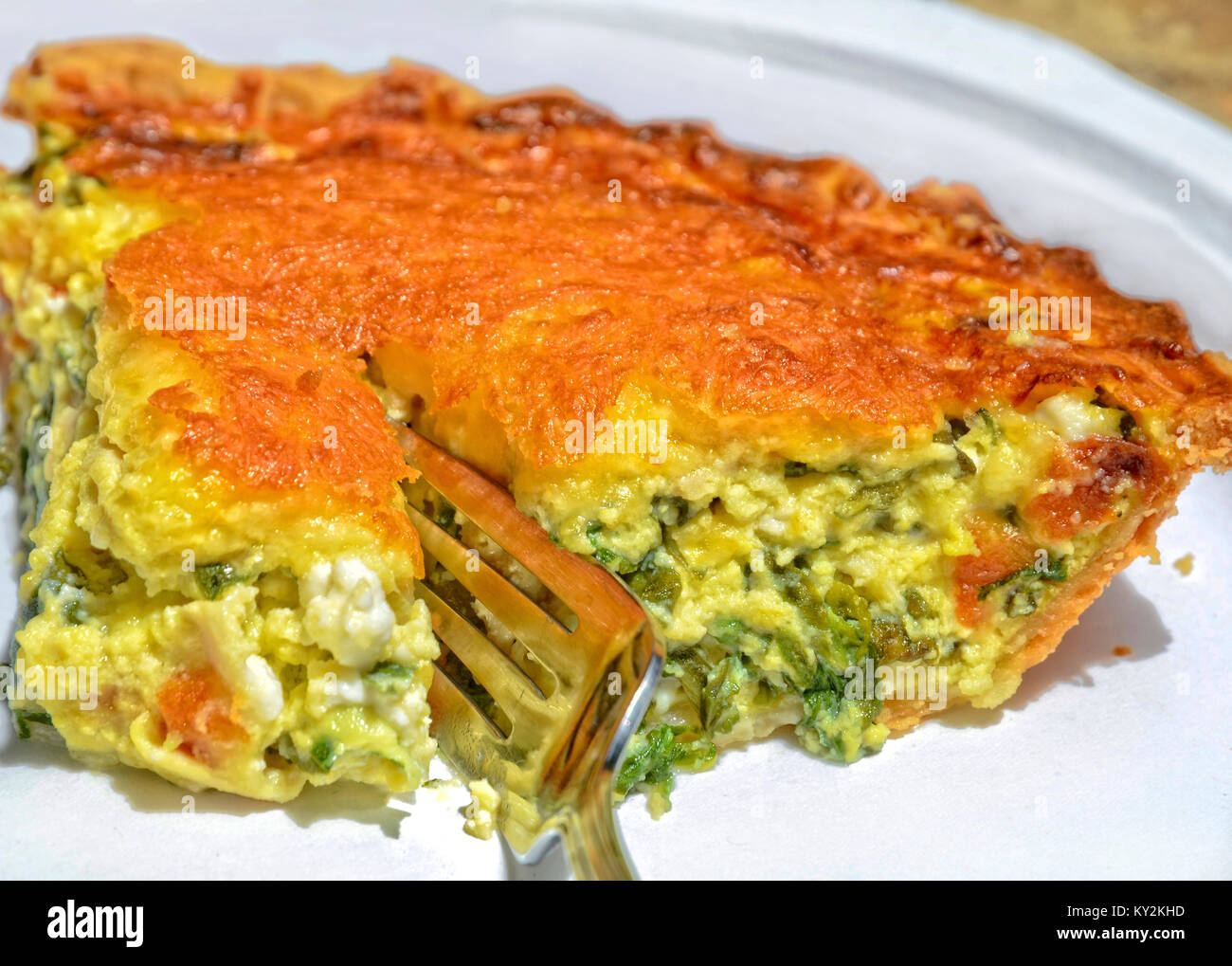 Closeup of a slice of quiche with spinach and cheese sliced with a fork. Stock Photo