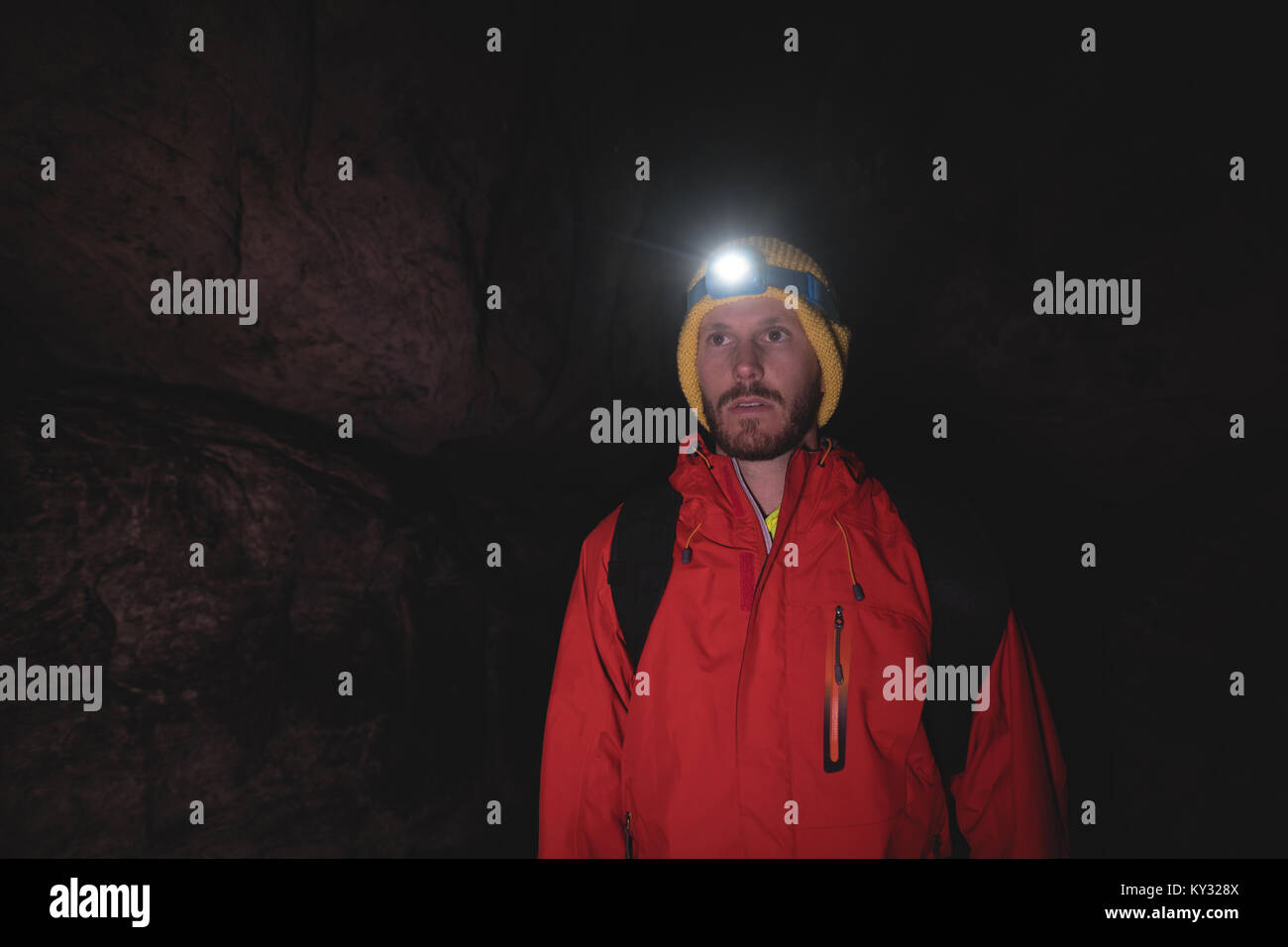 Hiker standing inside the dark cave wearing head torch Stock Photo