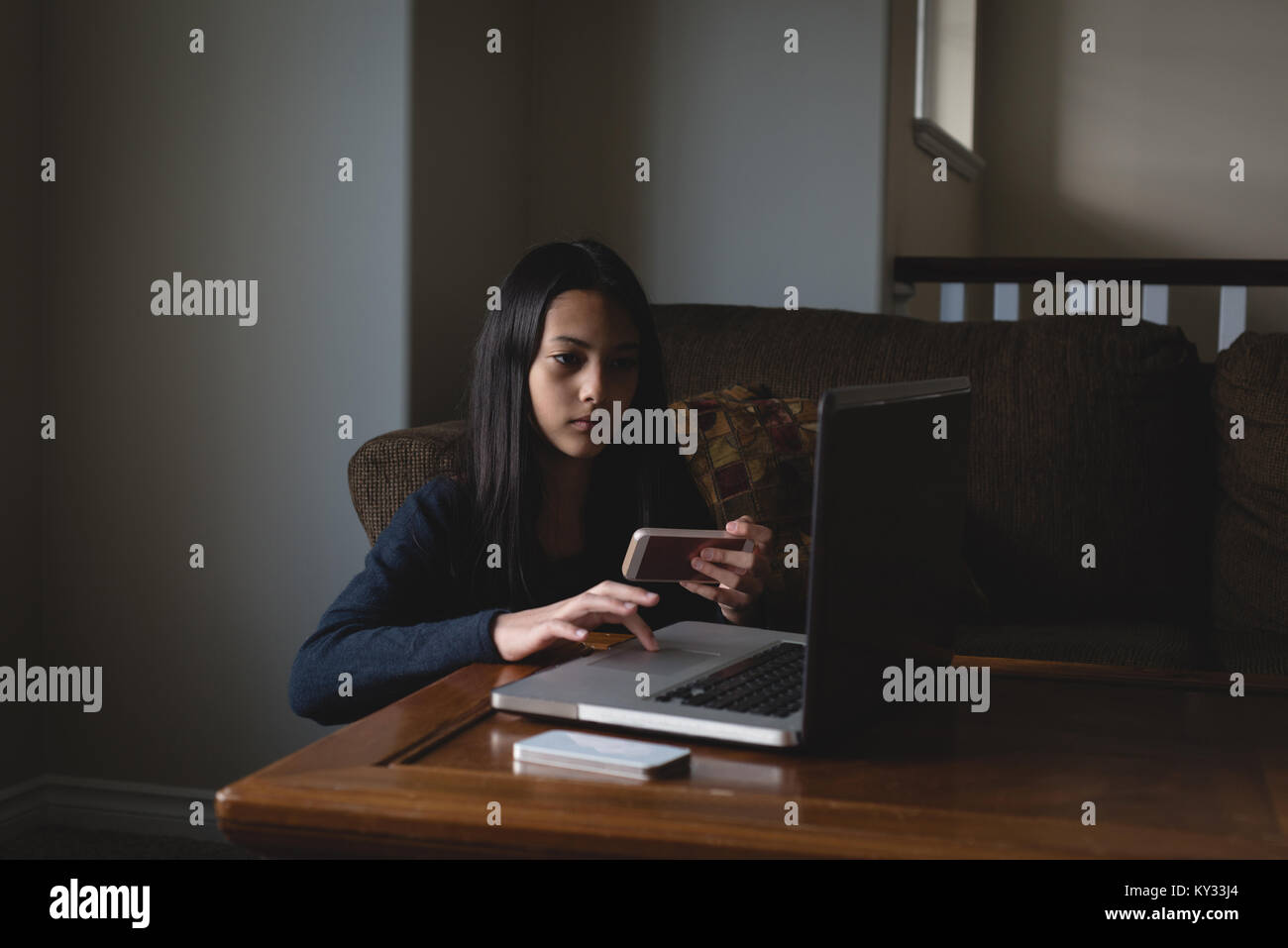 Girl using laptop and mobile phone in living room Stock Photo
