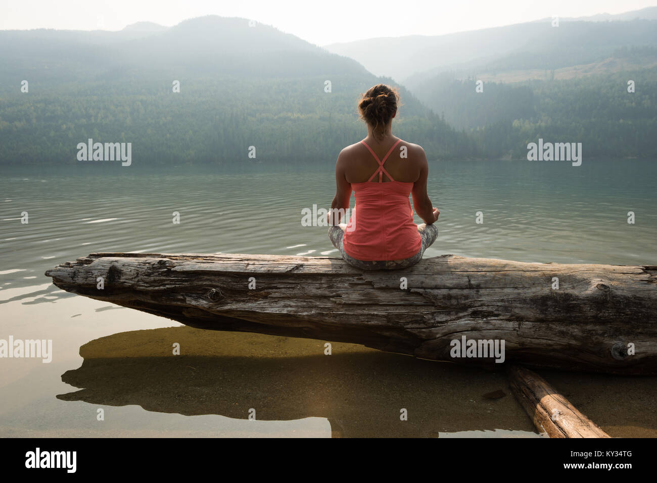 Fit woman sitting in meditating posture on a fallen tree trunk Stock Photo