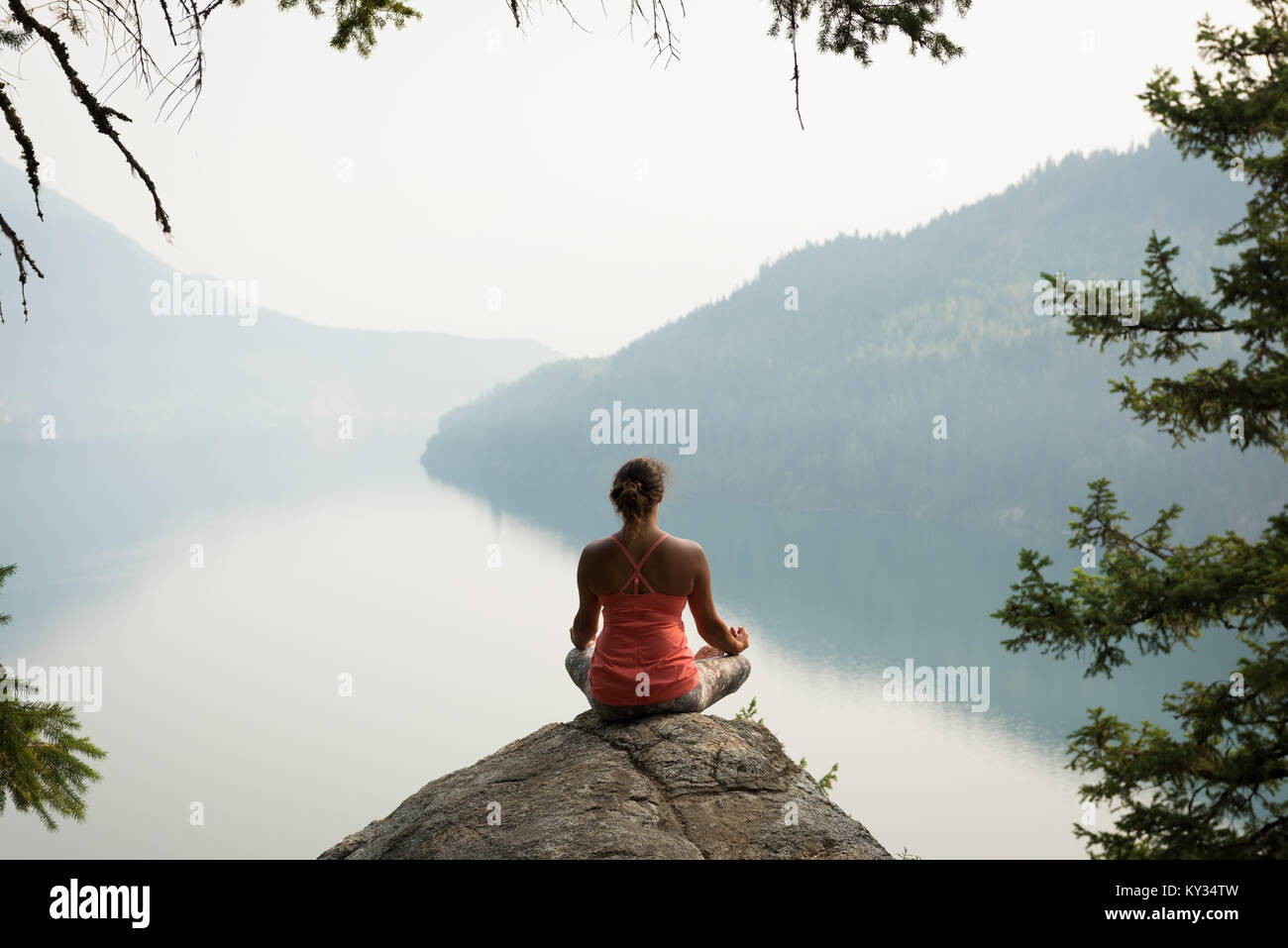 Fit woman sitting in meditating posture on the edge of a rock Stock Photo