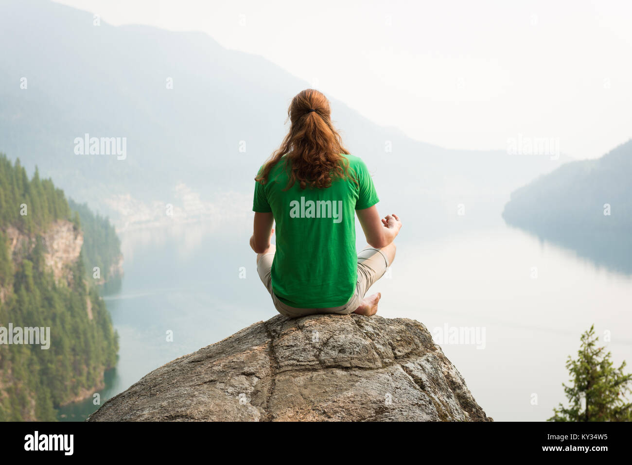 Fit man sitting in meditating posture on the edge of a rock Stock Photo