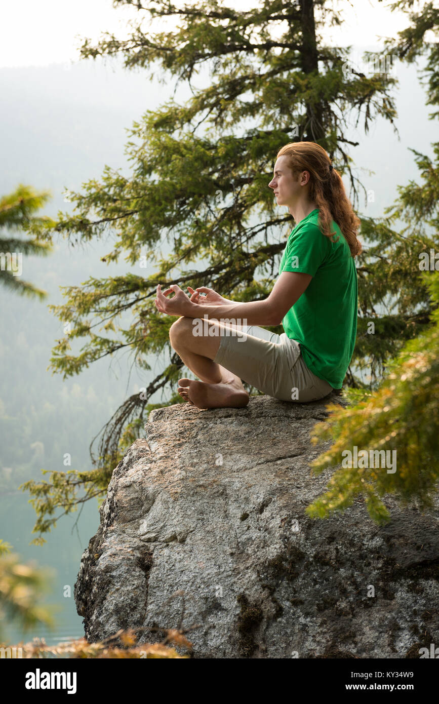 Fit man sitting in meditating posture on the edge of a rock Stock Photo