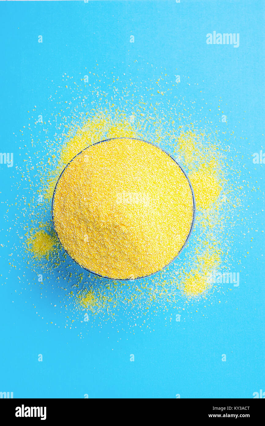 Bowl with Heap of Dry Uncooked Vibrant Yellow Color Polenta Spilled on Light Blue Background. Top View. Creative Image. Sun Imitation. Healthy Diet Me Stock Photo