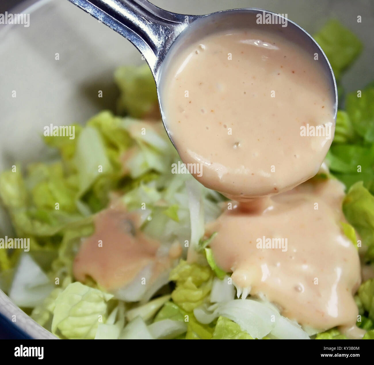 Tablespoon measure of creamy thousand island dressing being poured over fresh garden salad Stock Photo