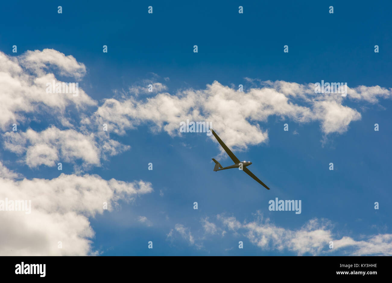 A Glider flying in bleu sky with big white clouds. The glider is a plane that has no engine Stock Photo