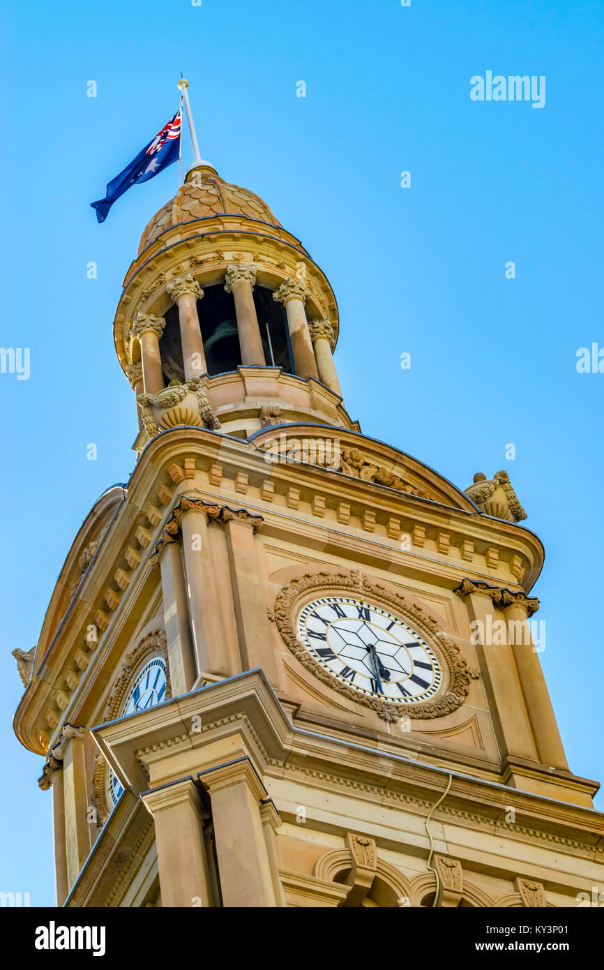 Clock Tower of Town Hall, Sydney city. Australian flag on top of tower of historic Town Hall building, blue sky. Stock Photo