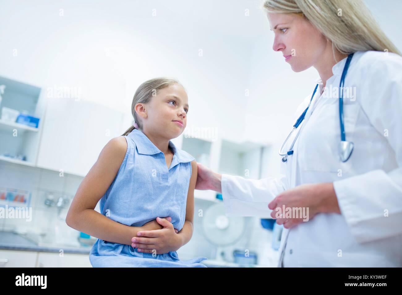 Girl clutching tummy, doctor with hand on her shoulder. Stock Photo