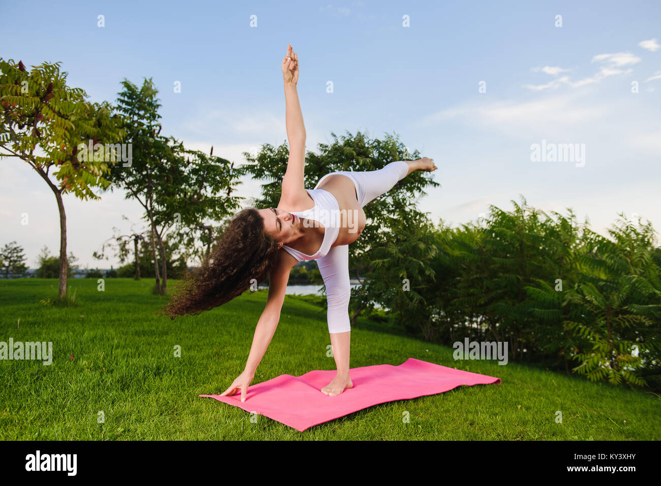 Pregnant woman doing prenatal yoga on nature. Ardha candrasana, pose of the half moon. Woman in park on grass. wide angle. Stock Photo