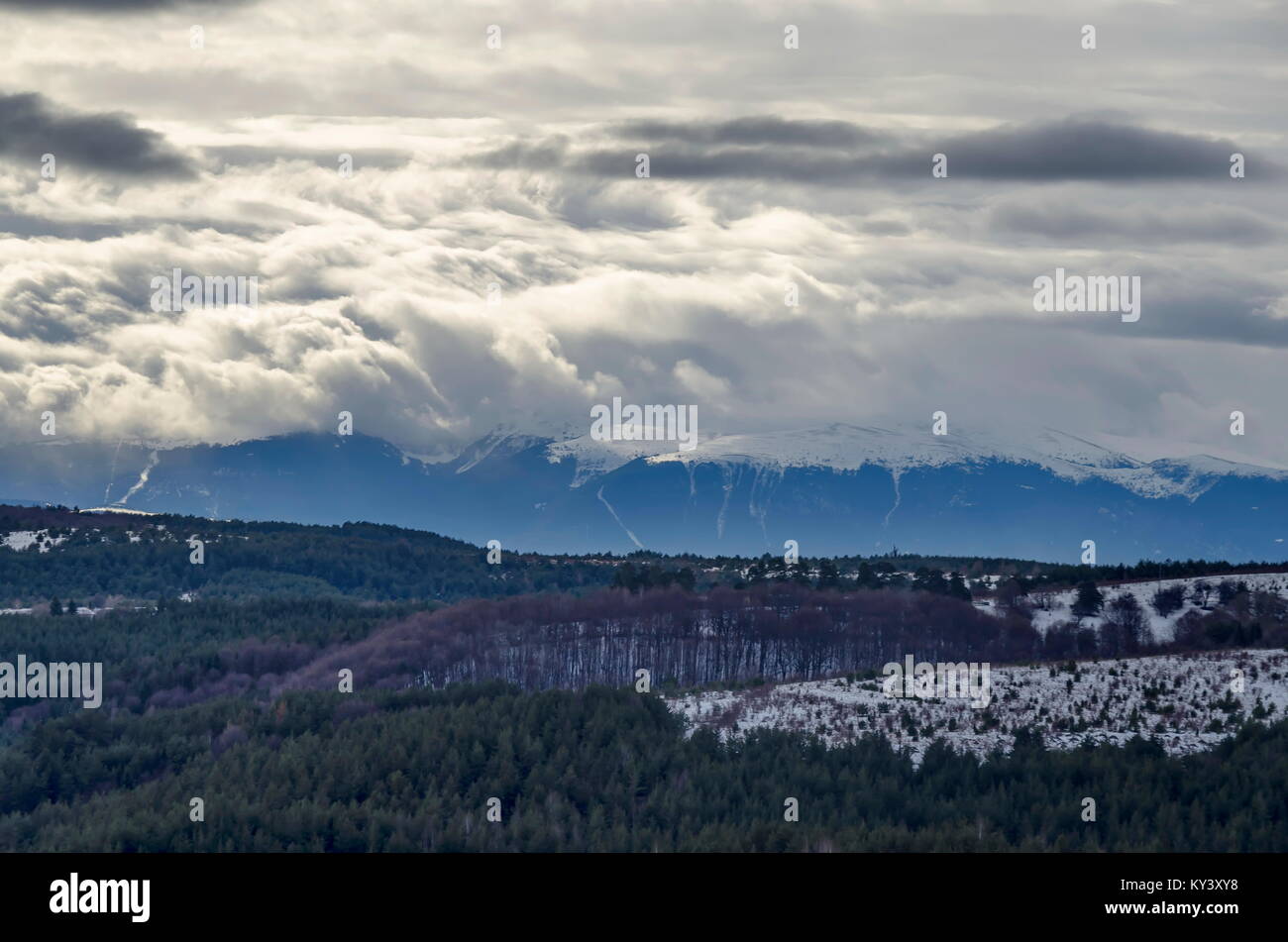 Majestic view of cloudy sky, winter mountain, snowy glade, conifer and deciduous forest from Plana mountain toward Rila mountain, Bulgaria, Europe Stock Photo
