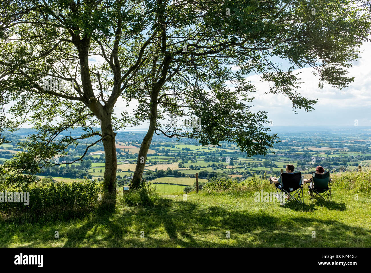 Young couple sitting on folding camping chairs and enjoying panoramic views from Coaley Peak picnic site and Viewpoint,Dursely, Gloucestershire, UK Stock Photo
