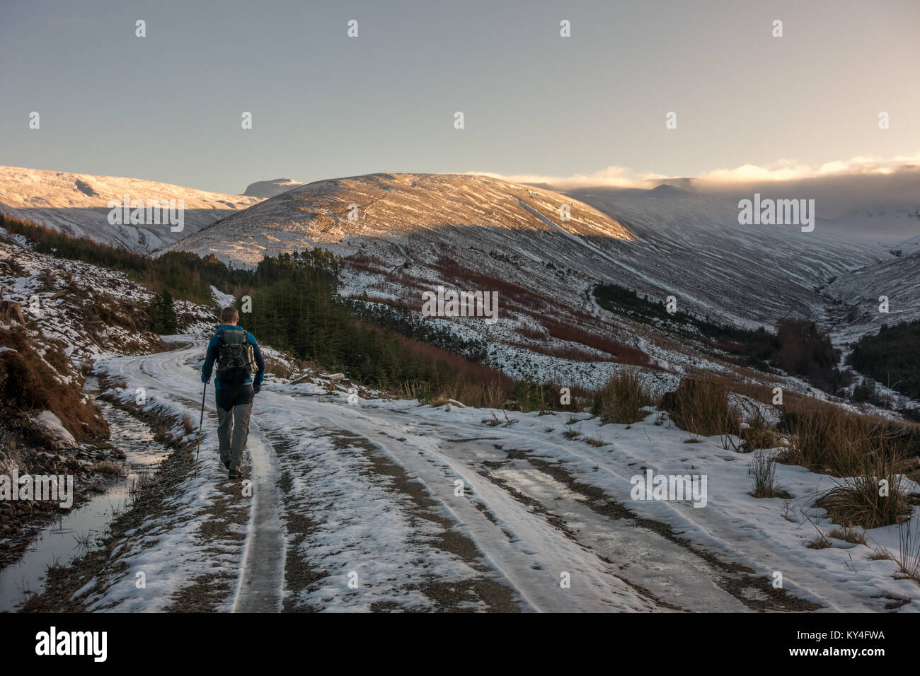 Hiker in icy and snowy winter conditions walking along the track