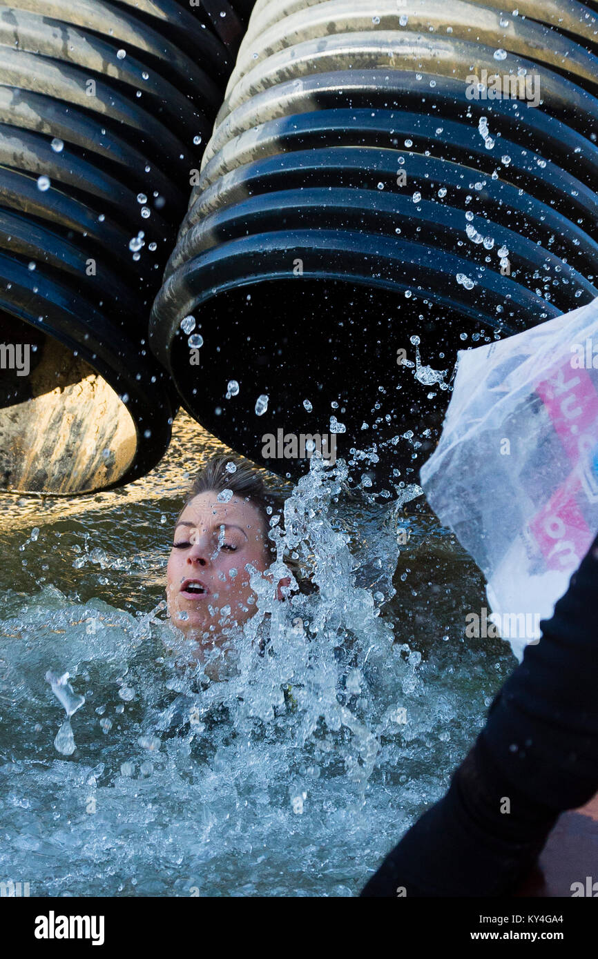 Sussex, UK. A young woman splashes into the 'Arctic Enema' obstacle, a pool full of ice water, during a Tough Mudder event. Stock Photo