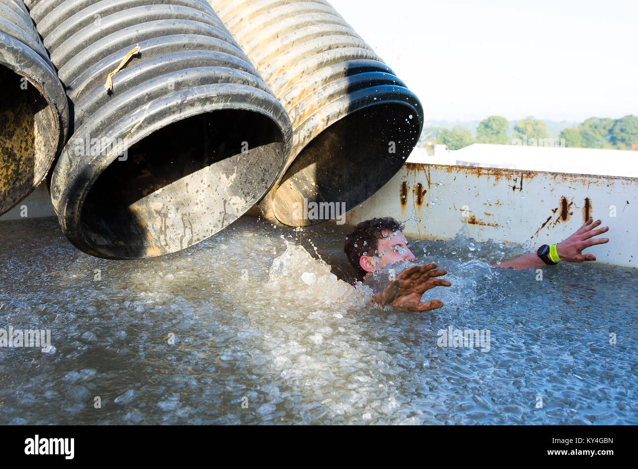 Sussex, UK. A male competitor splashes into the 'Arctic Enema' obstacle – a freezing cold pool of ice water – during a Tough Mudder event. Stock Photo