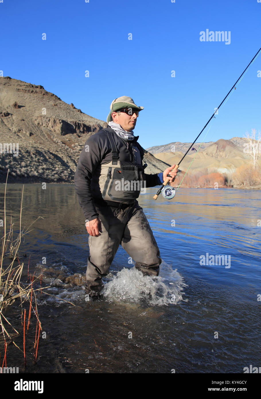 fisherman wading in river with fly rod Stock Photo