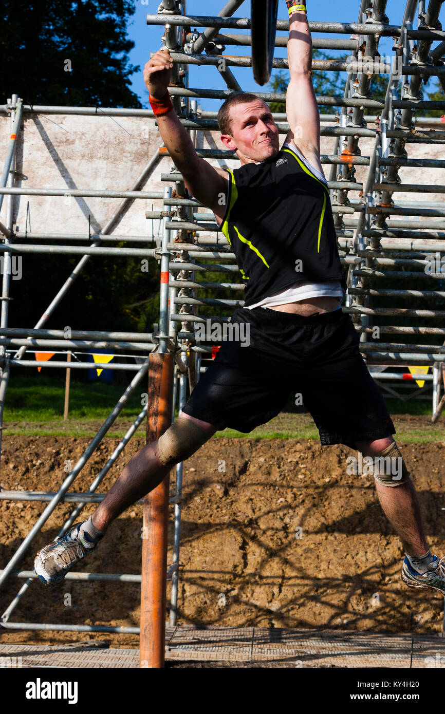 Sussex, UK. A male competitor pulls a determined face as he swings across the Hangin' Tough obstacle during a Tough Mudder event. Stock Photo