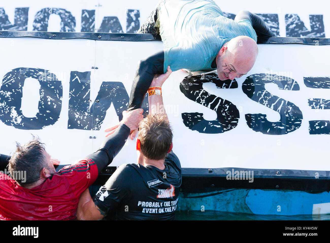 Sussex, UK. Two men pull a third over an hurdle on the Block Ness Monster obstacle during a Tough Mudder event. Stock Photo