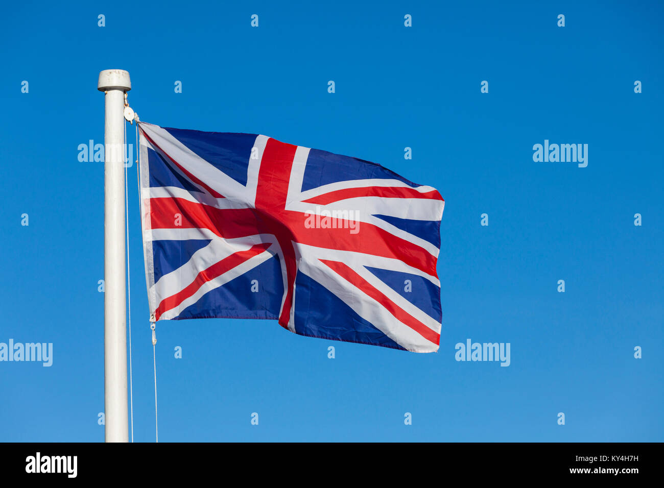 Union Jack flag and flagpole on a bright blue sky background blowing in ...