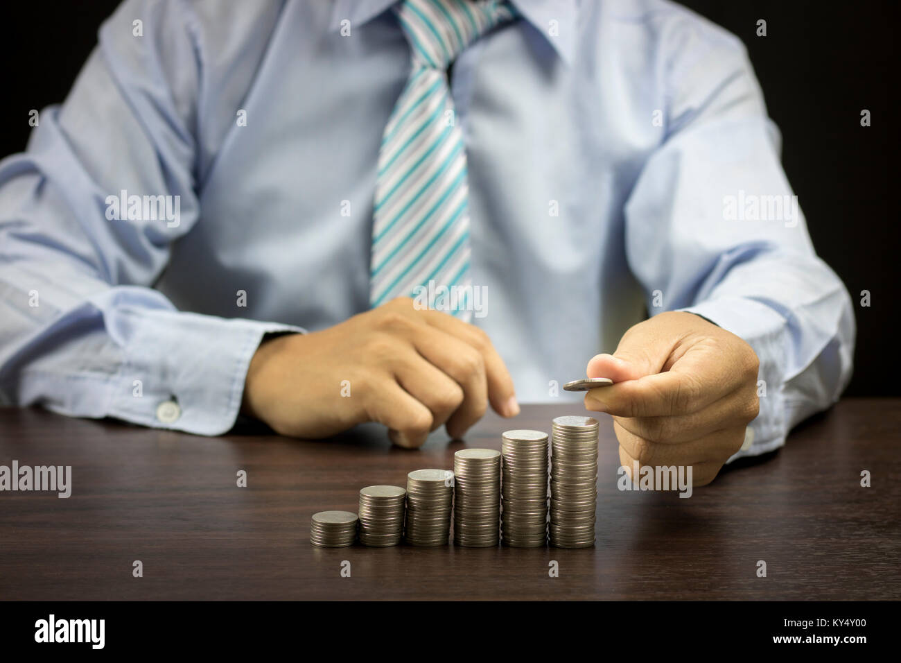 business man stacked coins on dark wood background, concept as investor, finace and capital banking Stock Photo