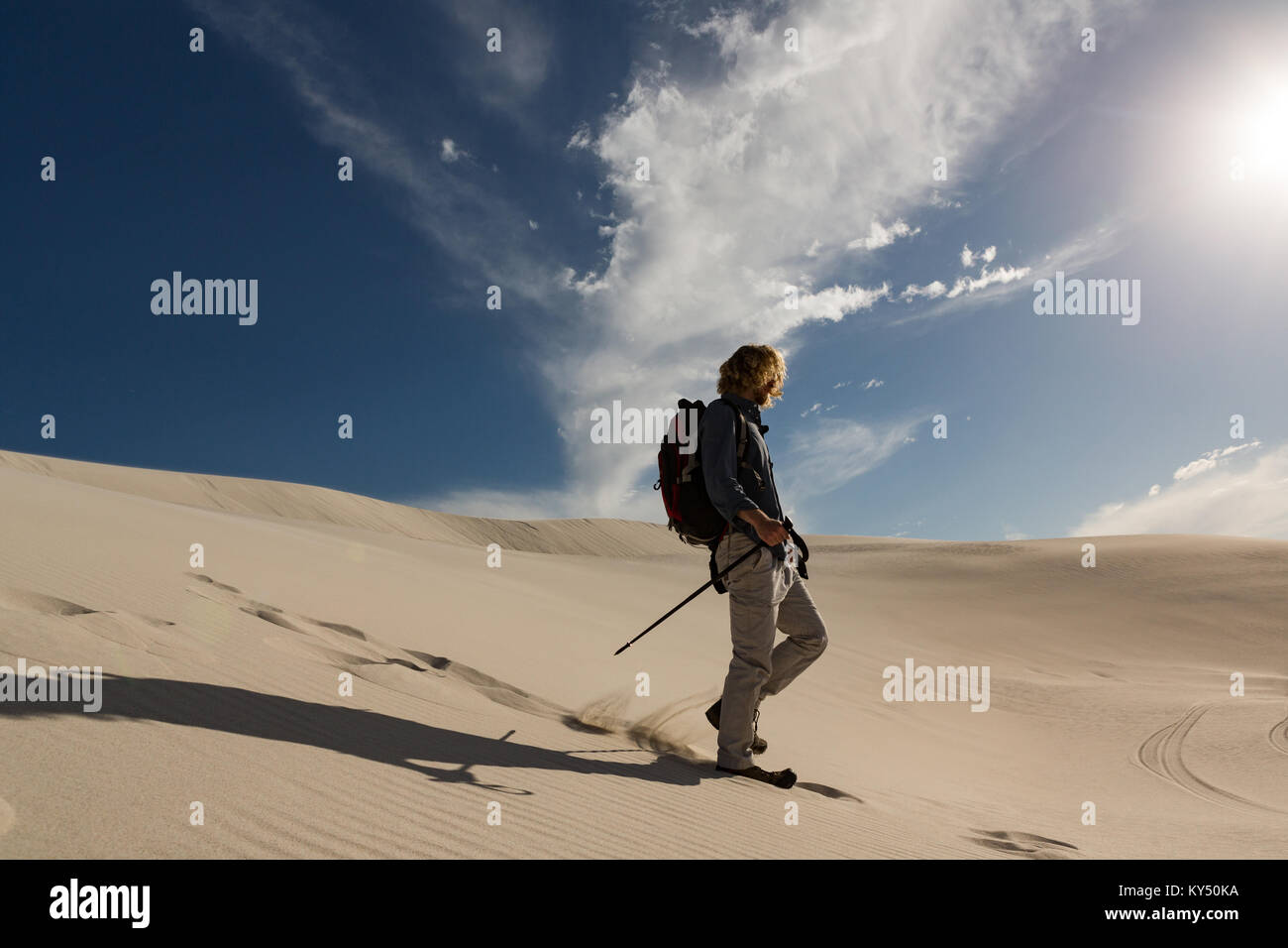 Male hiker with trekking pole walking on sand Stock Photo