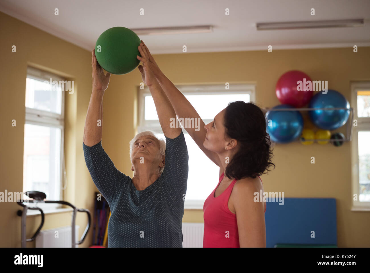 Female therapist assisting senior woman with ball Stock Photo