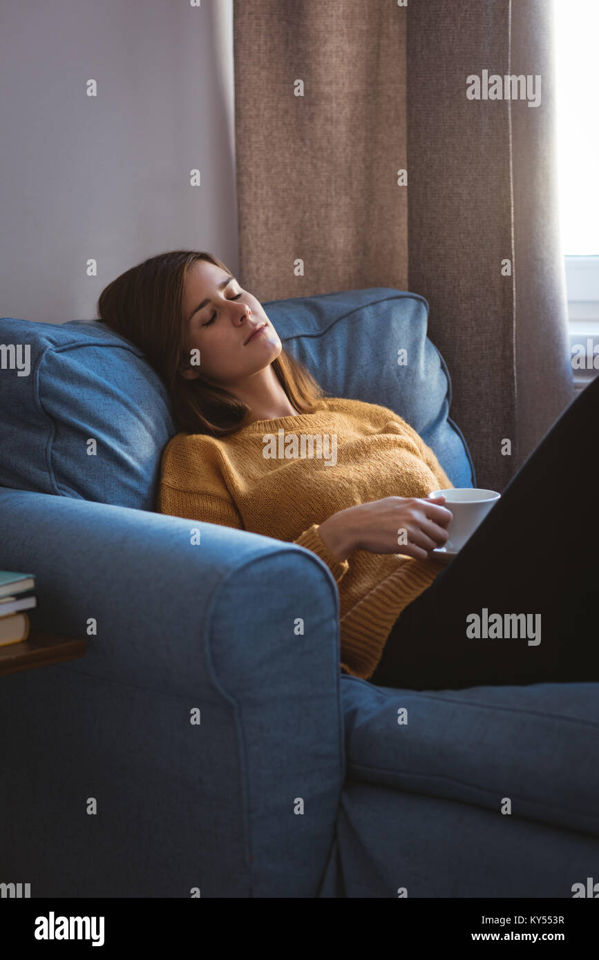 Young woman relaxing on sofa holding a cup of coffee in living room Stock Photo