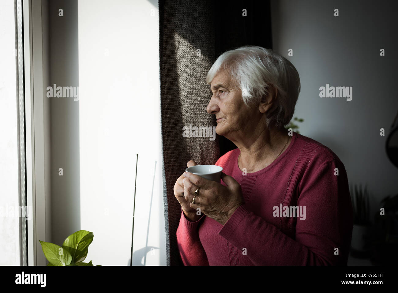 Senior woman having cup of tea while looking out of window Stock Photo