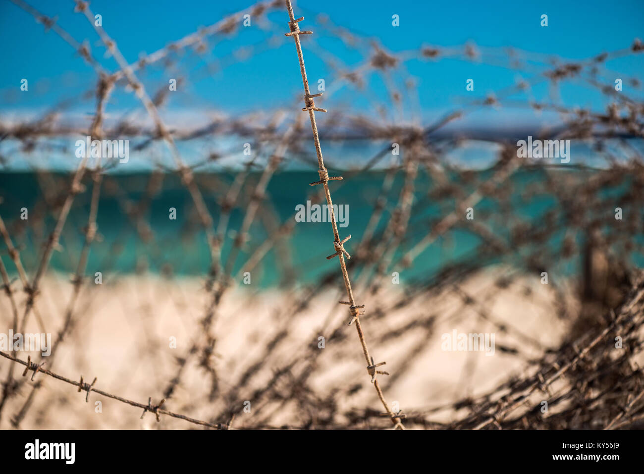 Old barbed wire infront of sea. Wire and blue sky with clouds. Safety fence of barbed wire against the blue sky and sea. Close-up. Stock Photo