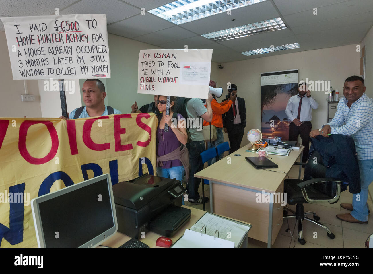 Usman Bhatti  stands in the office space of an unrelated company as he apparently phones police. UVW members hold placards which include a copy of a bounced cheque that he wrote. After 3 months of requests, Carlos has only got back £1000 of the £6500 he paid. Stock Photo