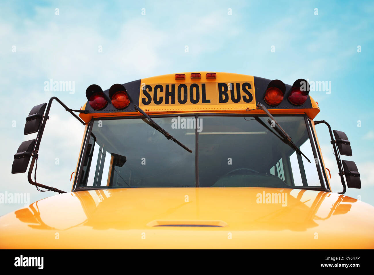 wide angle front view of a bright yellow orange school bus on a sunny summer day with clouds in the sky toned with a retro vintage instagram filter ap Stock Photo