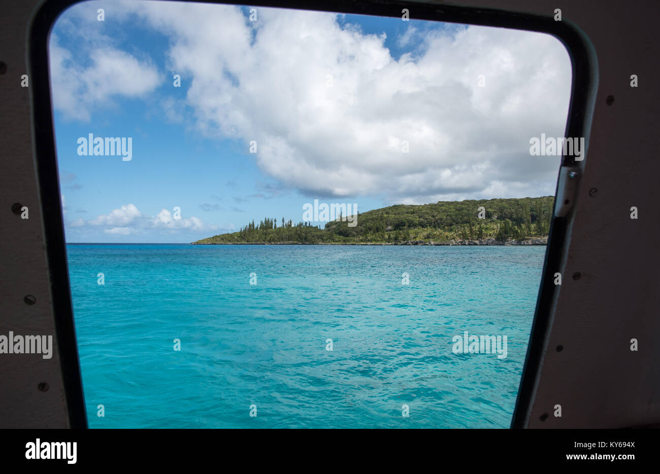 View through boat window over the stunning Pacific Ocean waters and lush, green forest at Tadine, Mare, New Caledonia Stock Photo