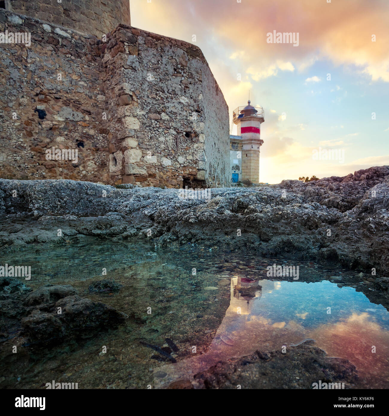 The castle of Brucoli and little lighthouse reflected in a puddle ...