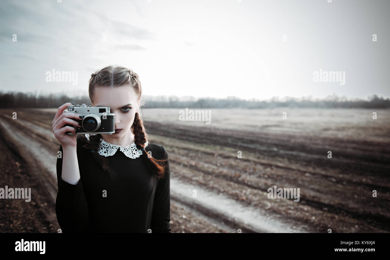 Serious young girl photographing by the old film camera. Outdoor portrait in the field Stock Photo