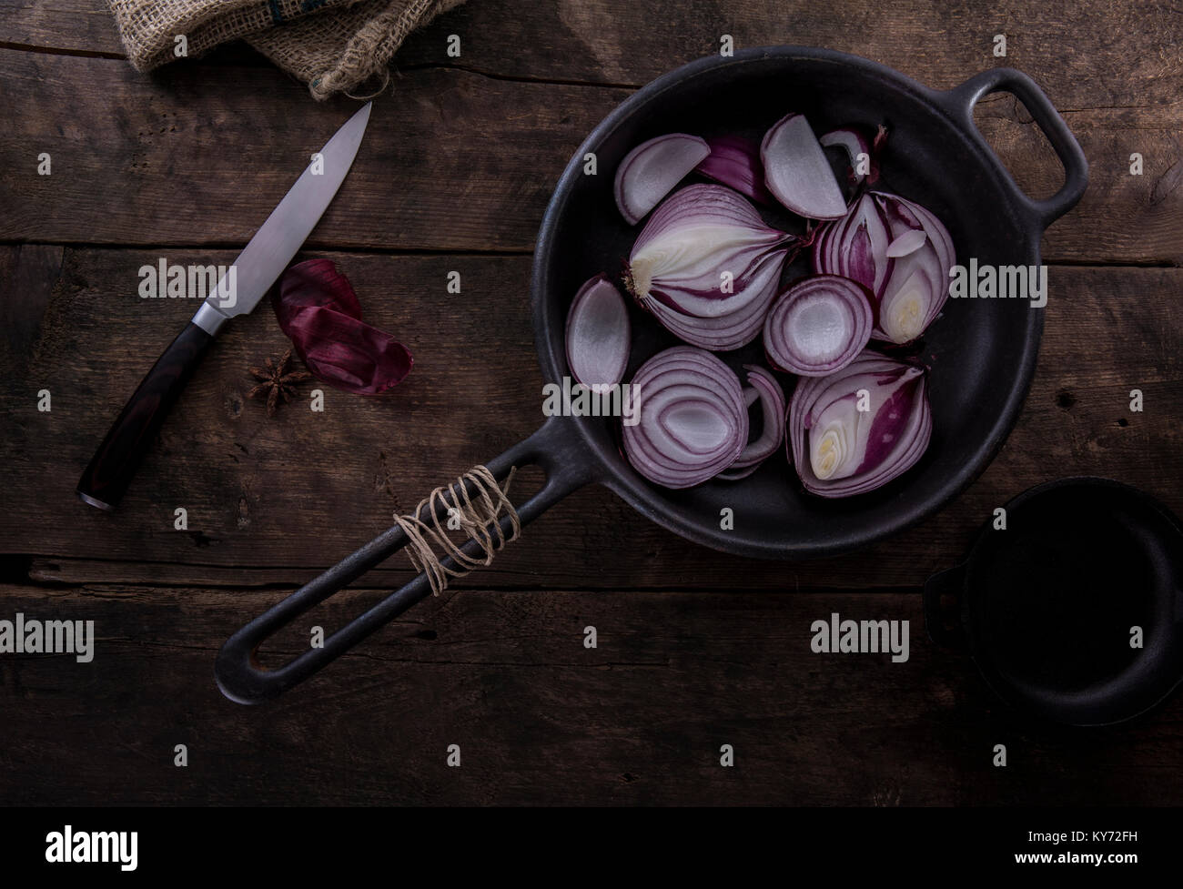 Red Onions in a cast iron frying pan on a rustic wooden table with a knife Stock Photo
