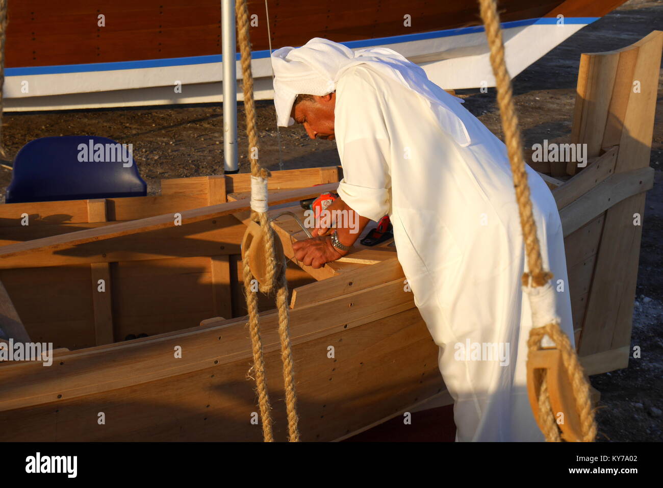 A Bahraini craftsman wearing a traditional dishdasha builds a tradional wooden dhow, Manama, Kingdom of Bahrain Stock Photo