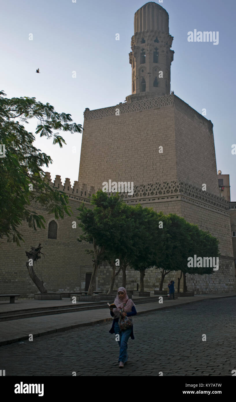 A young girl reading the Quran, while walking past a mosque on Al Moez street in Islamic Cairo Stock Photo