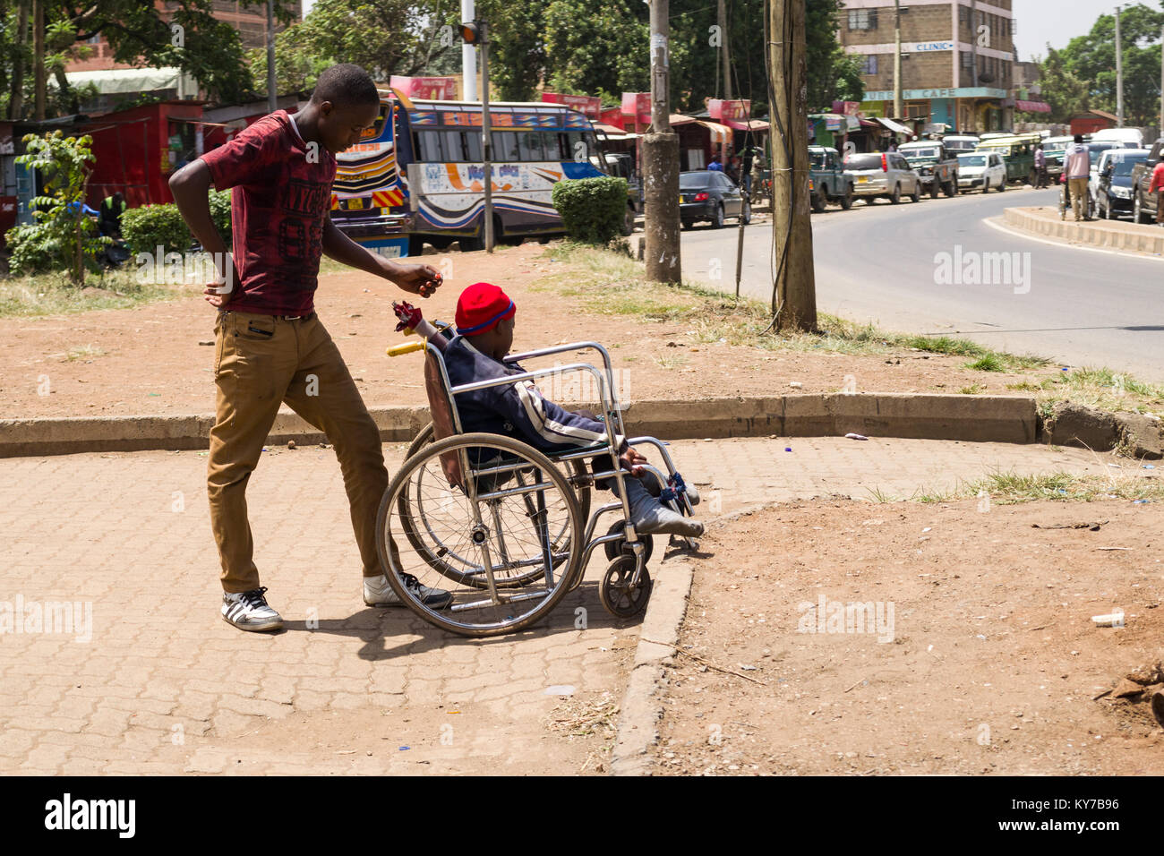 A man with a disabled person sat in a wheelchair wait by a busy road to beg for money, Nairobi, Kenya, East Africa Stock Photo