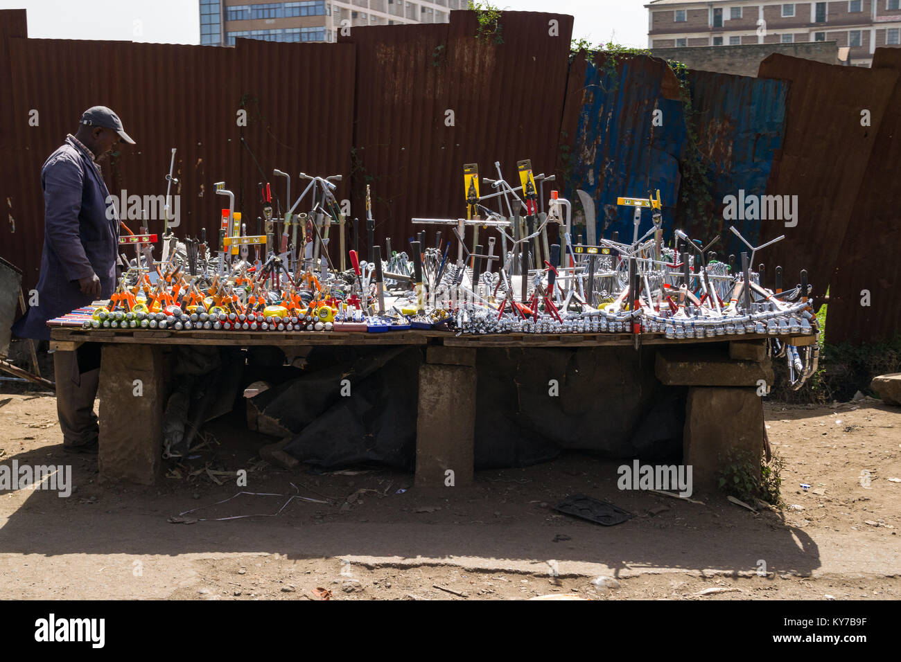 A Kenyan man stands by his roadside stall which has various work tools