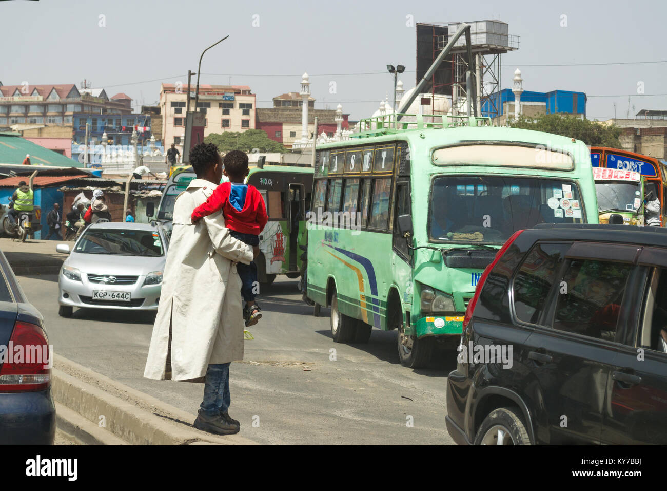 A Kenyan man holding his son waits to cross a busy road, Nairobi, Kenya, East Africa Stock Photo
