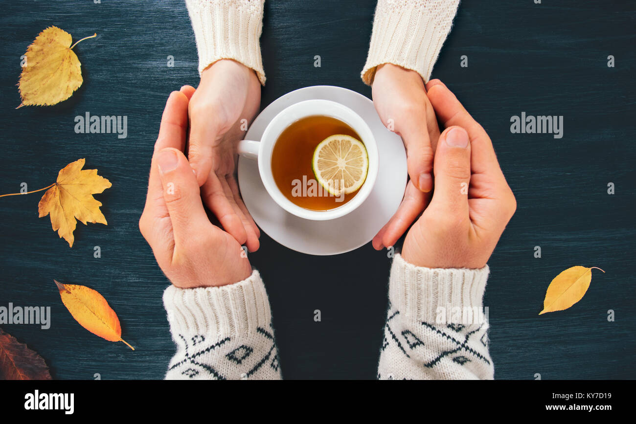 Couple Man and Woman in Love holding hands with hot tea lemon cup on dark wooden table with autumn leaves Romantic relationship feelings concept top v Stock Photo
