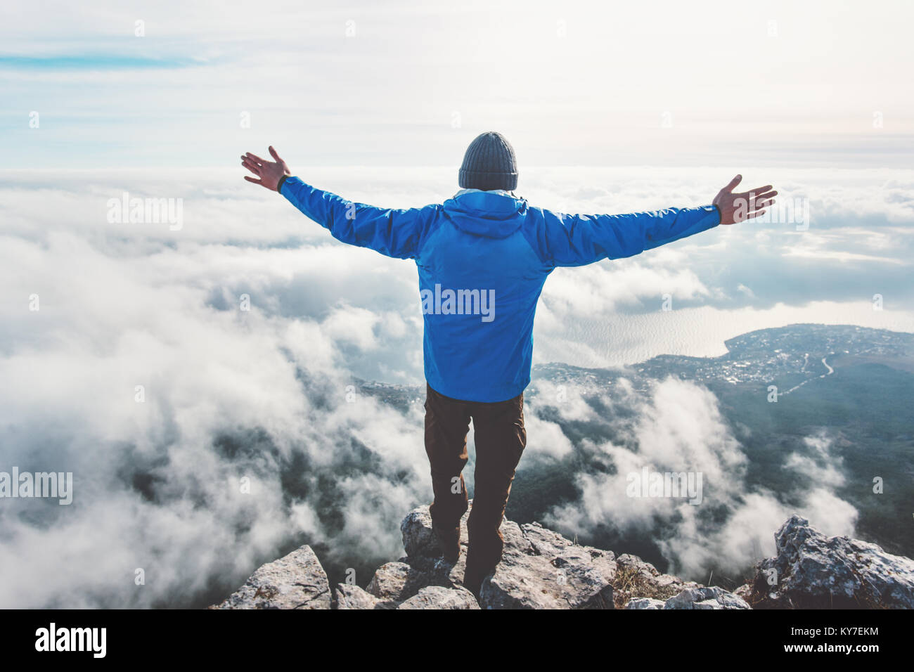 Man on mountain cliff enjoying aerial view hands raised over clouds Travel Lifestyle success concept adventure active vacations outdoor freedom emotio Stock Photo