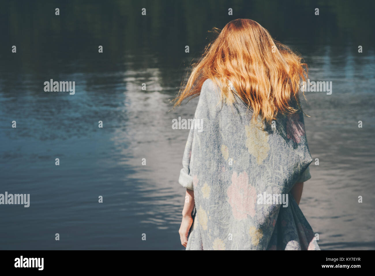 Young woman walking at river alone wearing long cardigan Fashion Lifestyle emotions concept red hair on wind Stock Photo