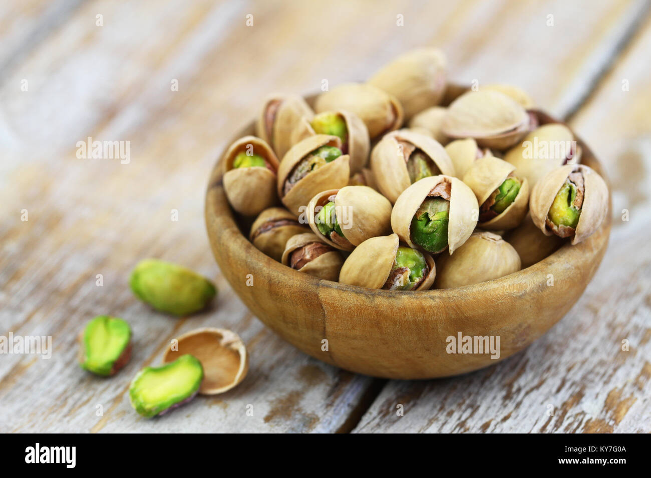 Pistachios with and without shell in bamboo bowl on rustic wooden surface Stock Photo